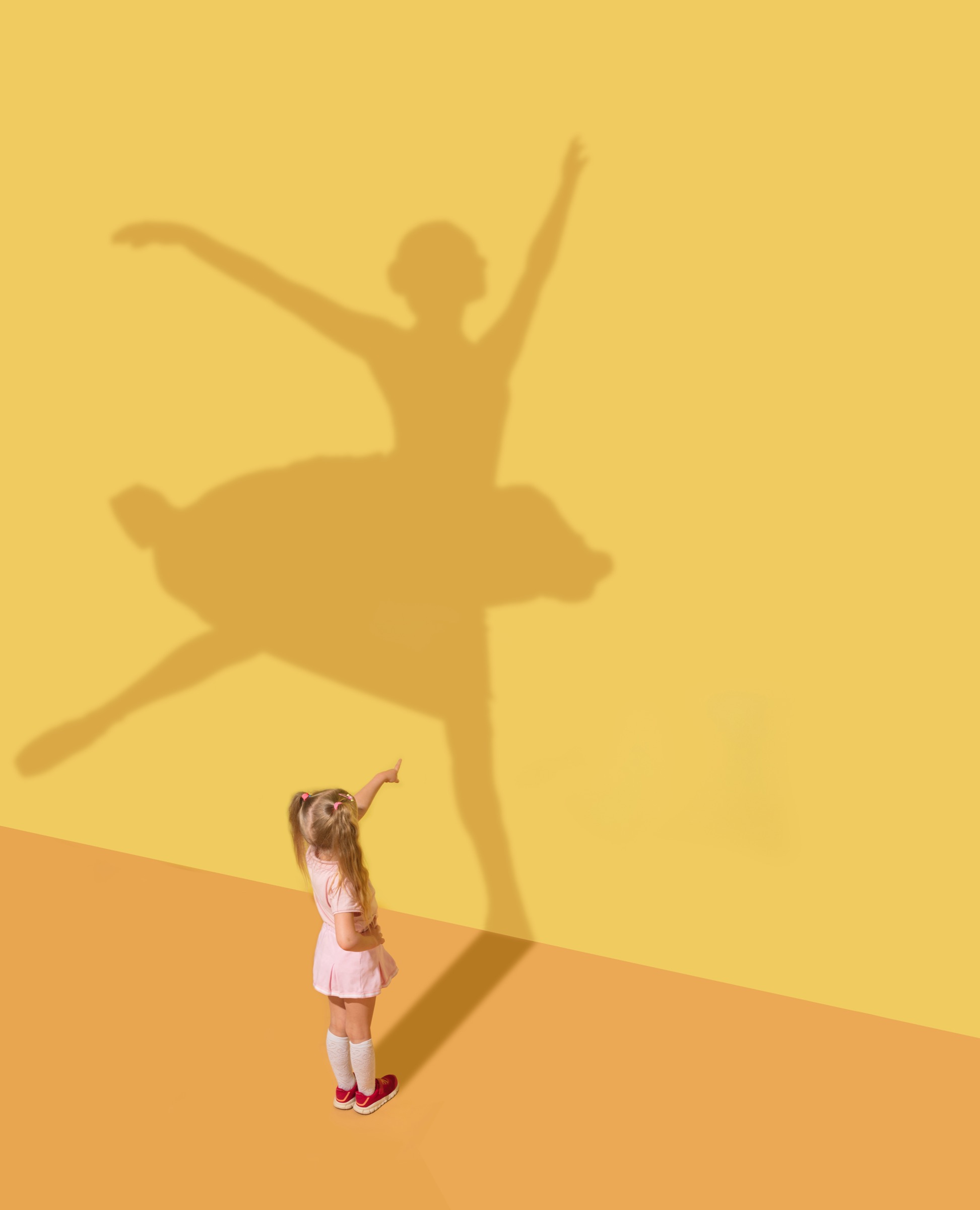 A child pointing at a ballerina shadow on a yellow studio wall