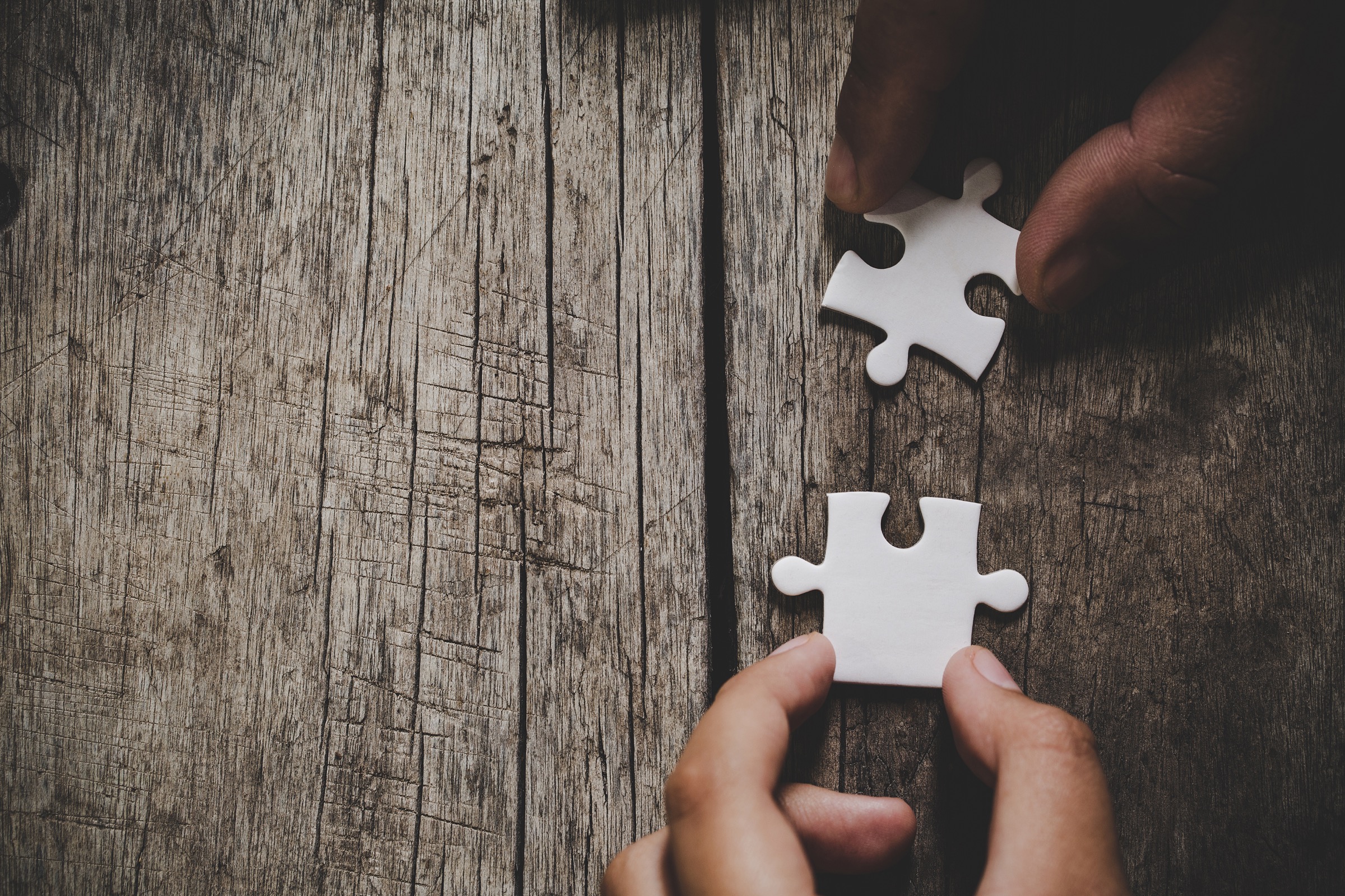 Hands connecting white puzzle pieces on a wooden table